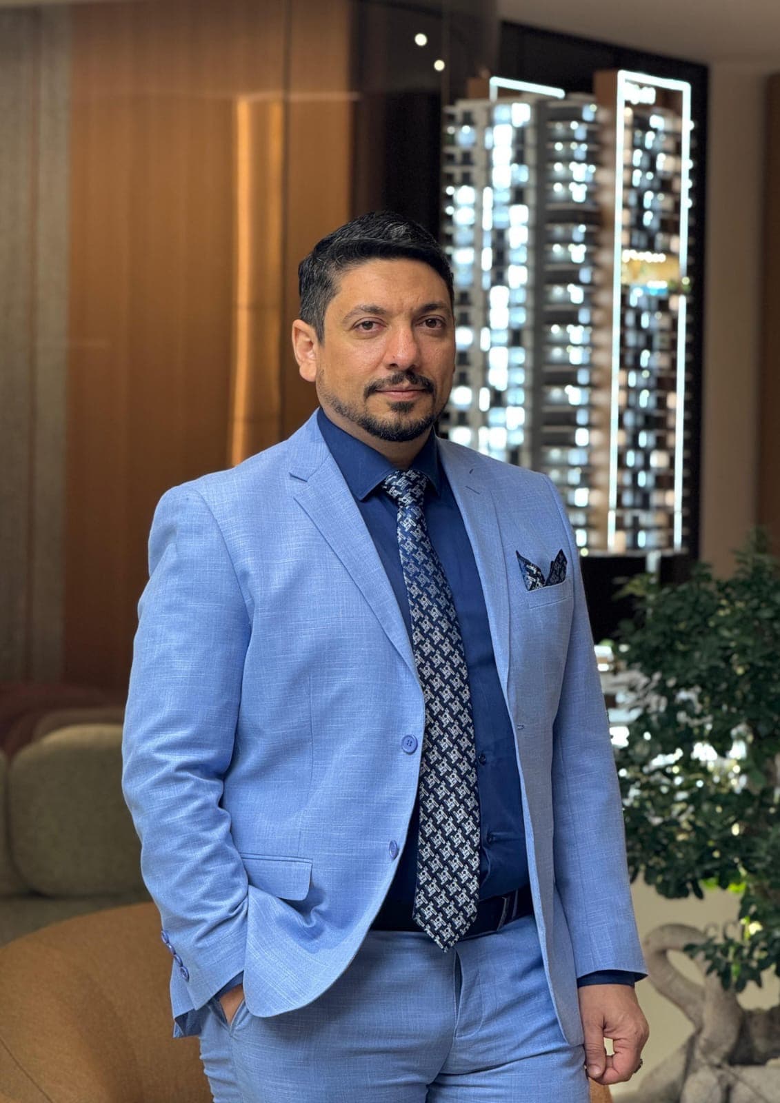 Weeam El Naggar standing in a Dubai real estate sales gallery, wearing a light blue suit